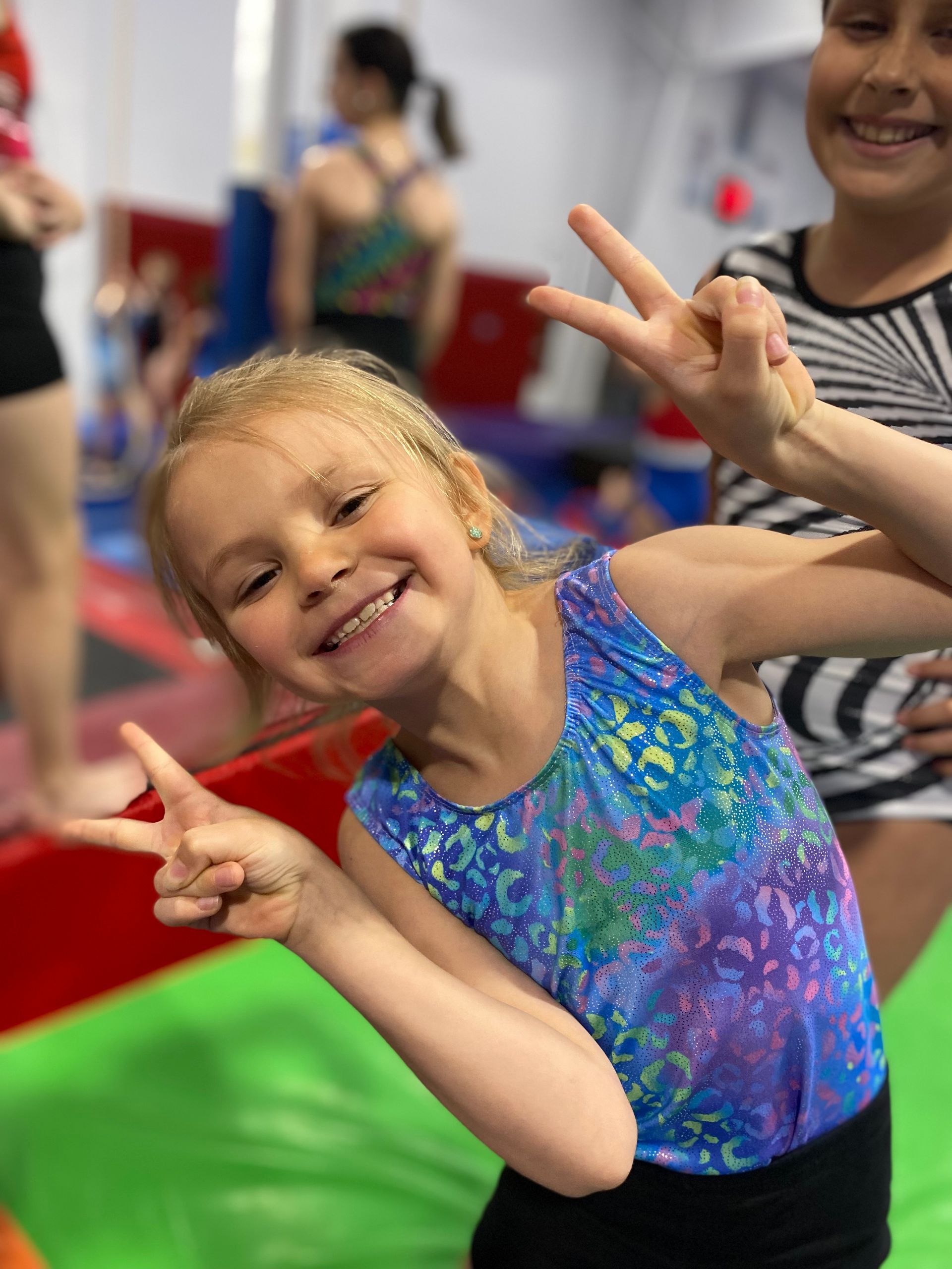 A little girl in a blue leotard is giving a peace sign.