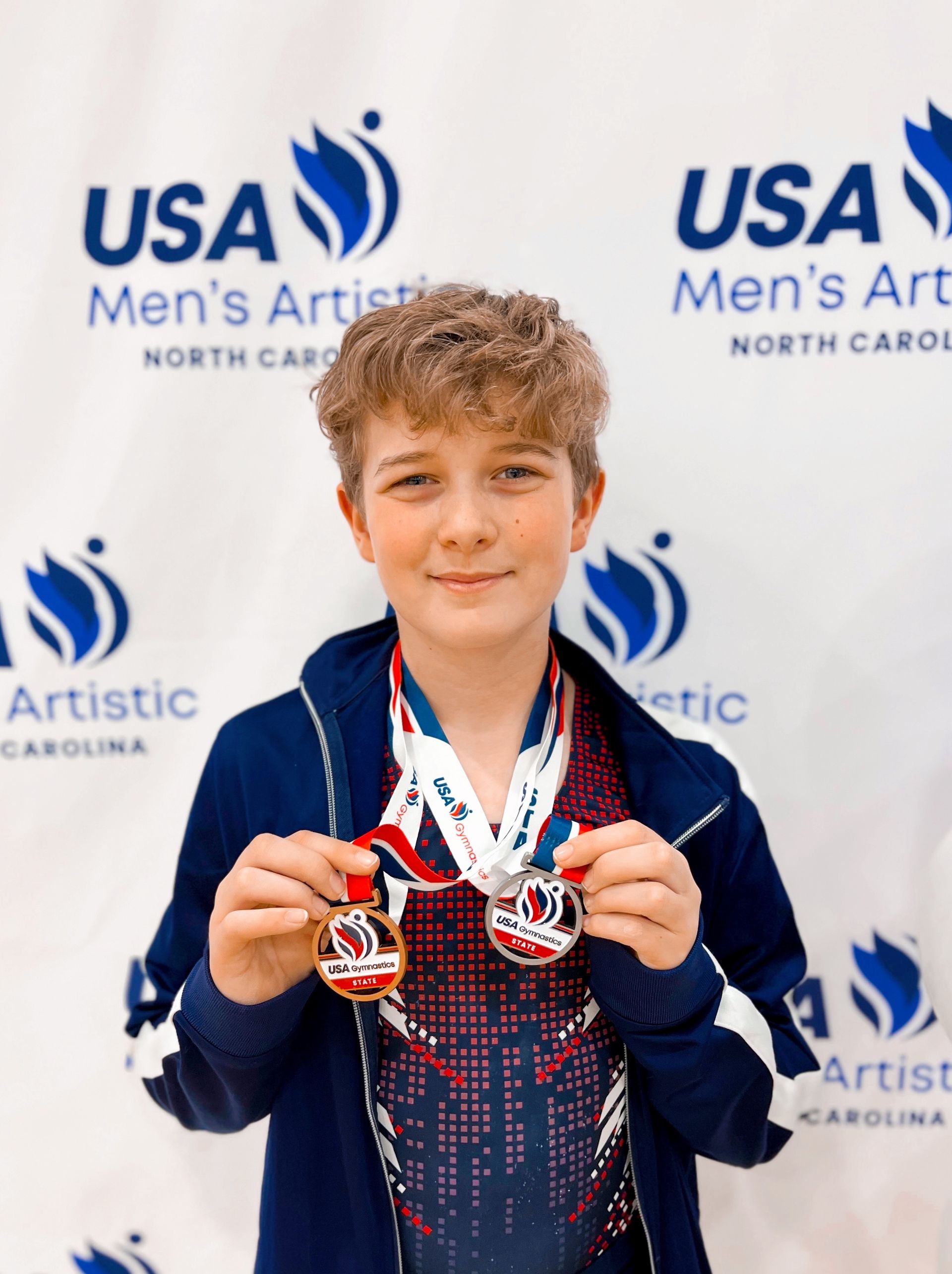 A young boy is holding two medals in front of a usa men 's artist banner