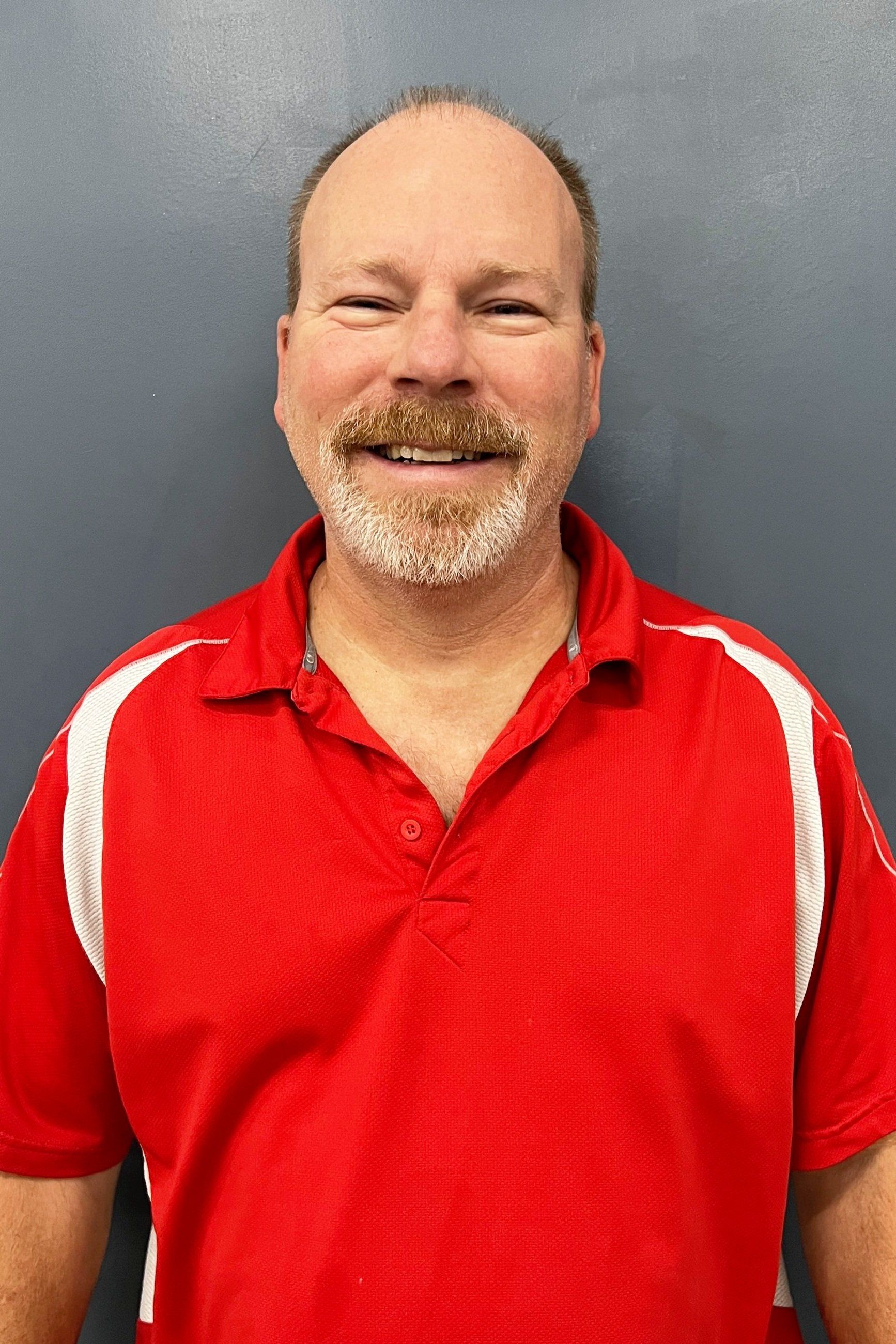 A man with a beard is wearing a red shirt and smiling.