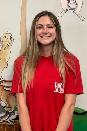 A woman in a red shirt is smiling in front of a painting of animals.