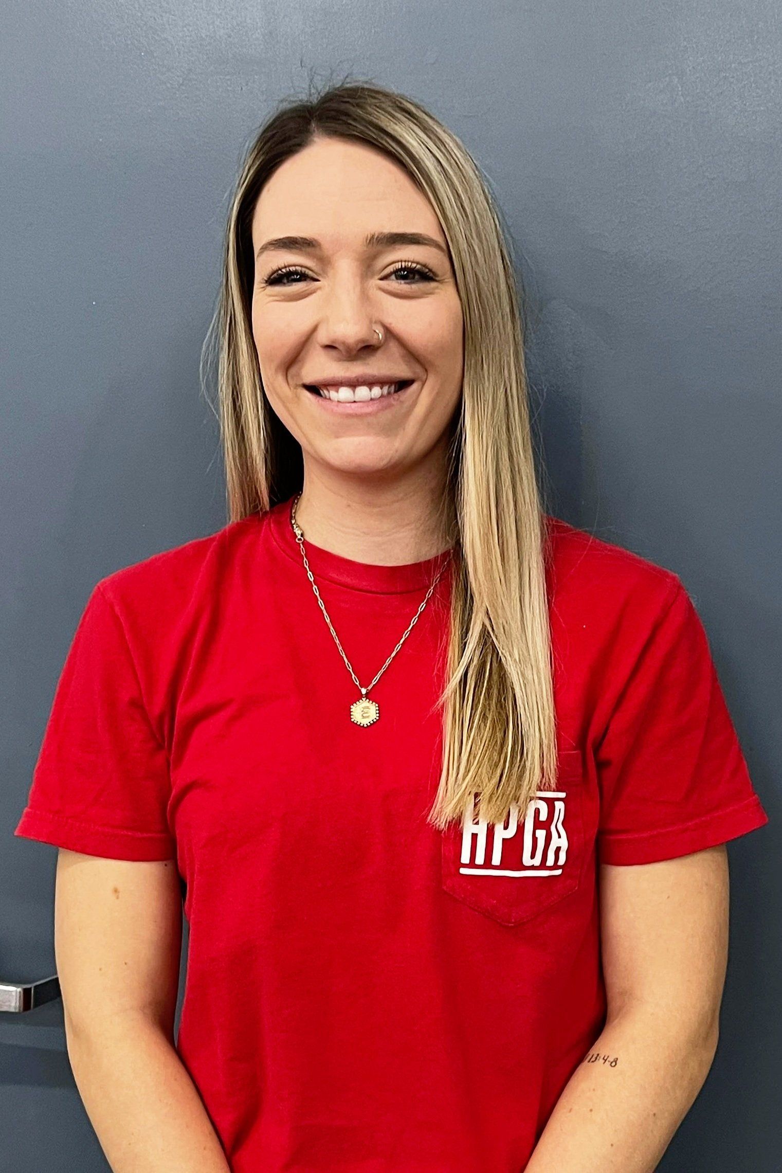 A woman wearing a red t-shirt and a necklace is smiling.