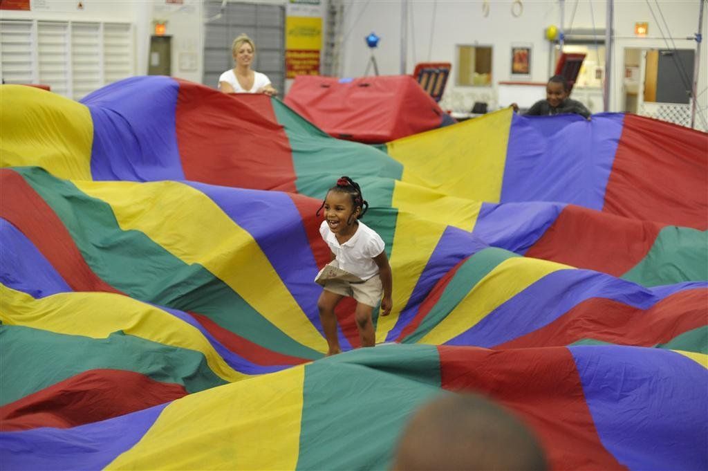 A little girl is running through a colorful parachute