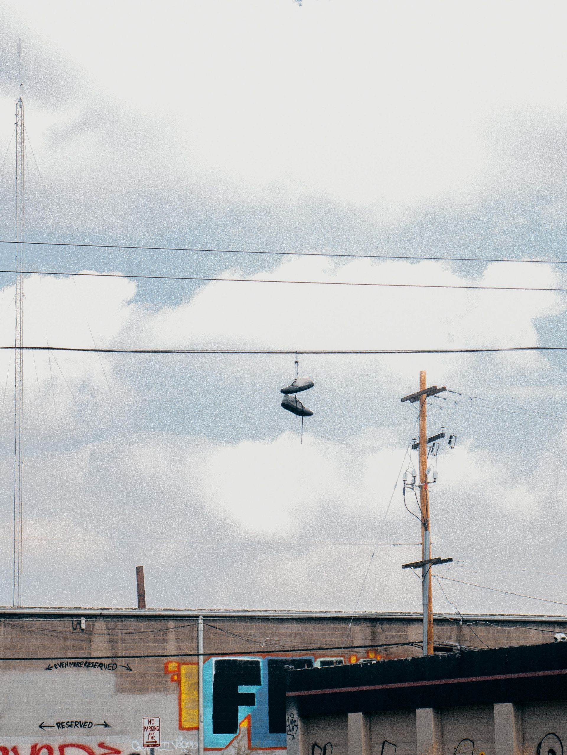 Shoes hanging from a power line above a building with graffiti, under a cloudy sky.