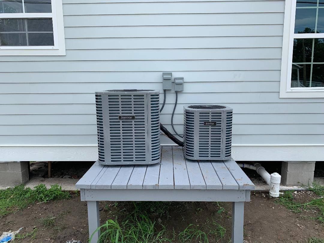 Two air conditioners are sitting on a small table outside of a house.