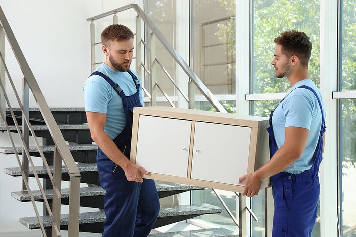 workers carrying cabinet at stairs in office