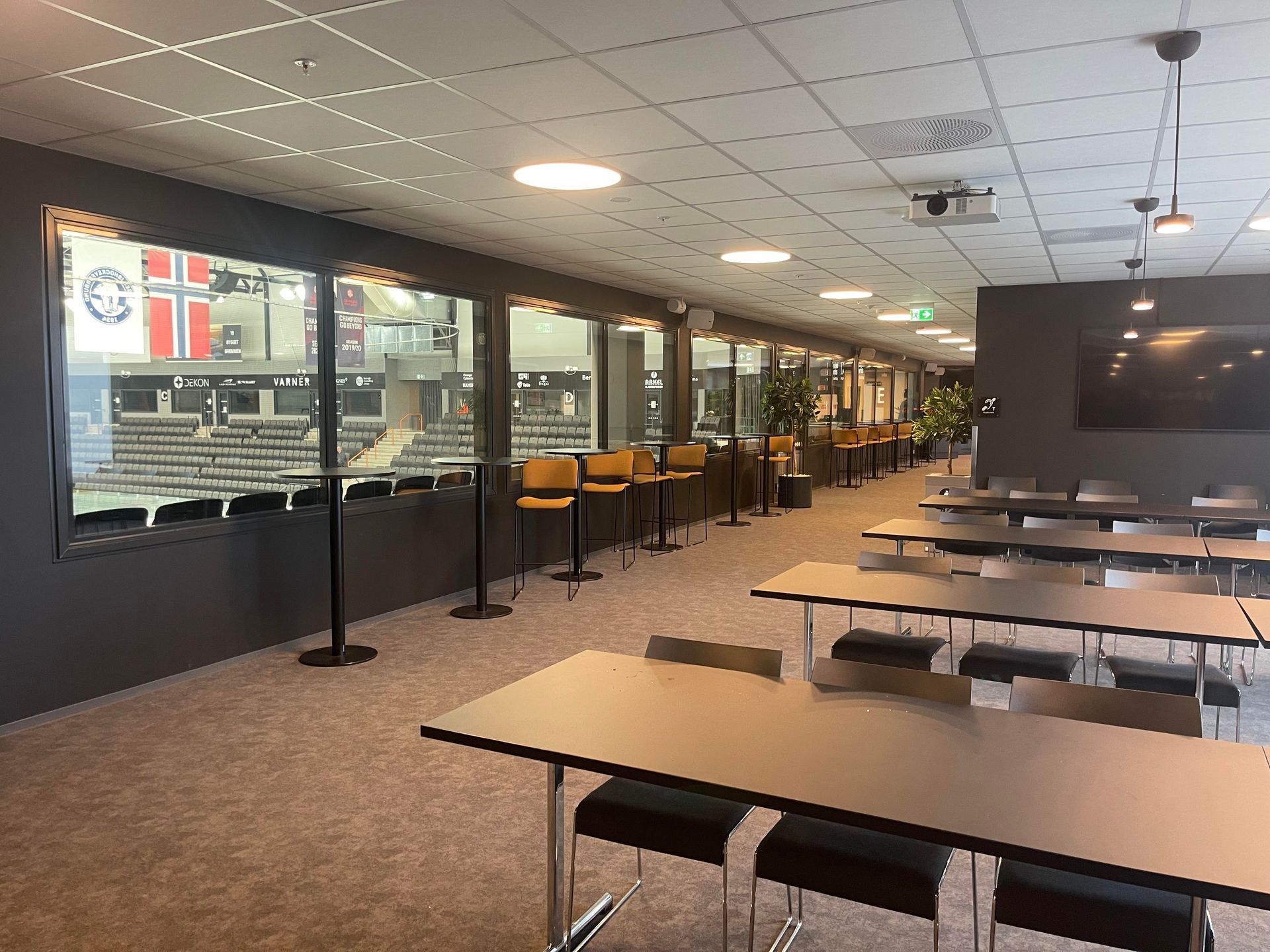 et langt rom med bord og stoler og et stort vindu.