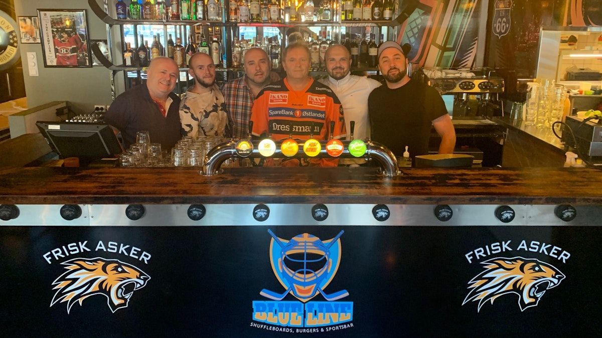 en gruppe menn poserer foran en bar.