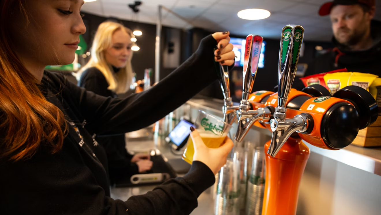 en kvinne skjenker øl i et glass på en bar.