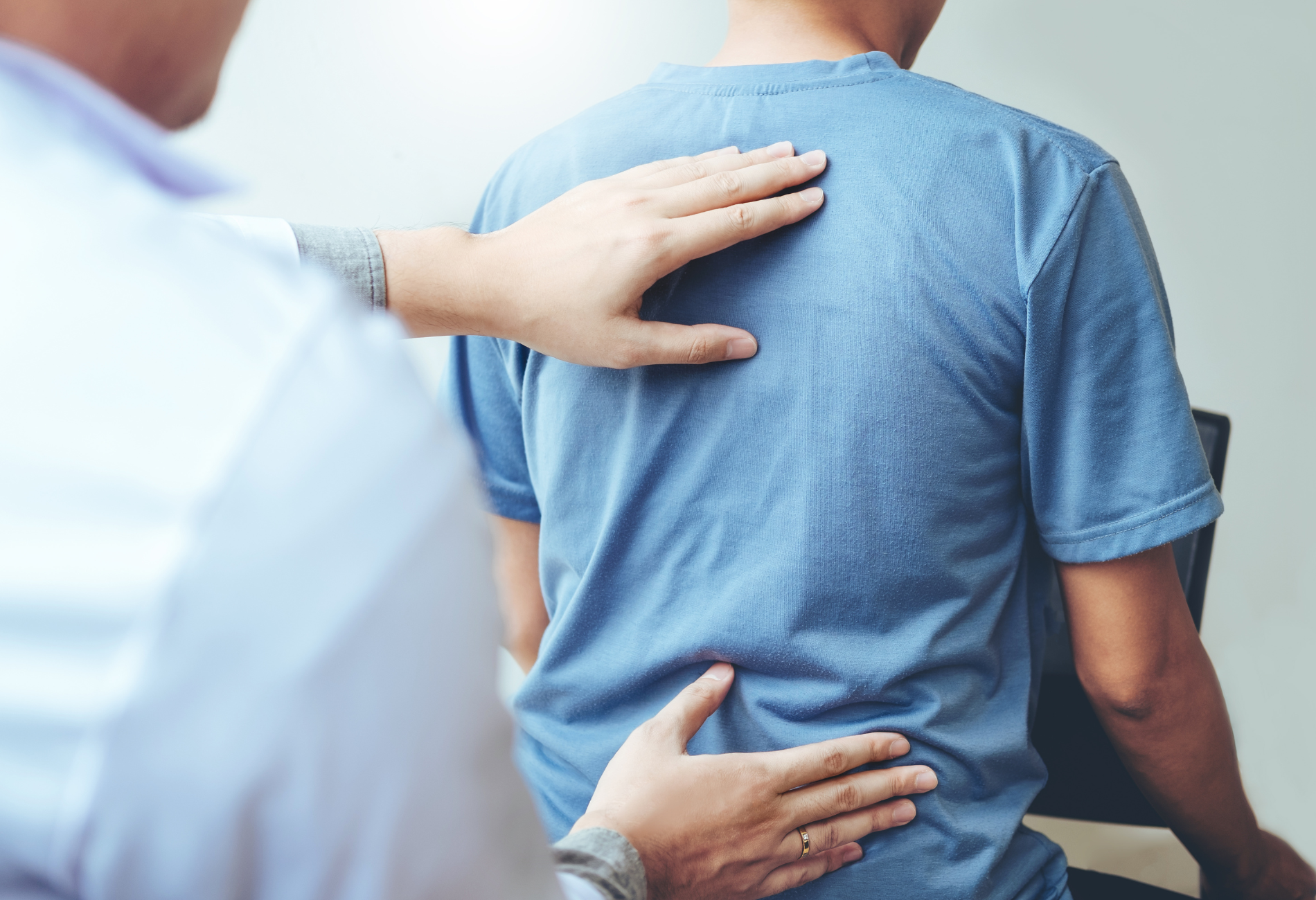 A man is sitting in a chair while a doctor examines his back.