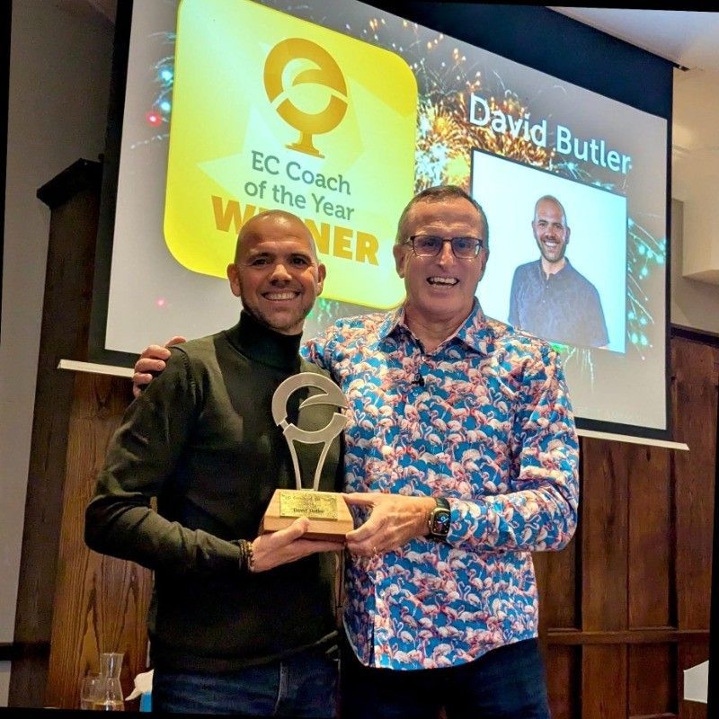 Two men are holding a trophy in front of a screen that says Bavid Butler
