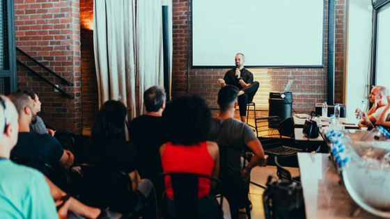 A group of people are sitting in front of a projector screen in a room.