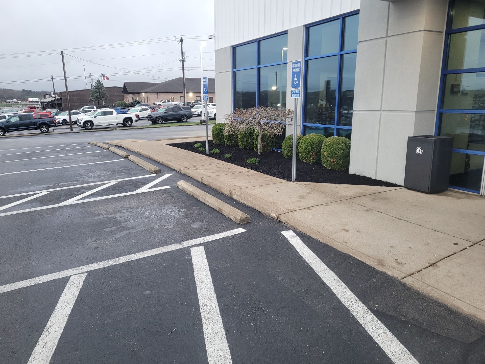 A parking lot featuring an accessible parking spot with signage in front of a building with a sidewalk and landscaping.