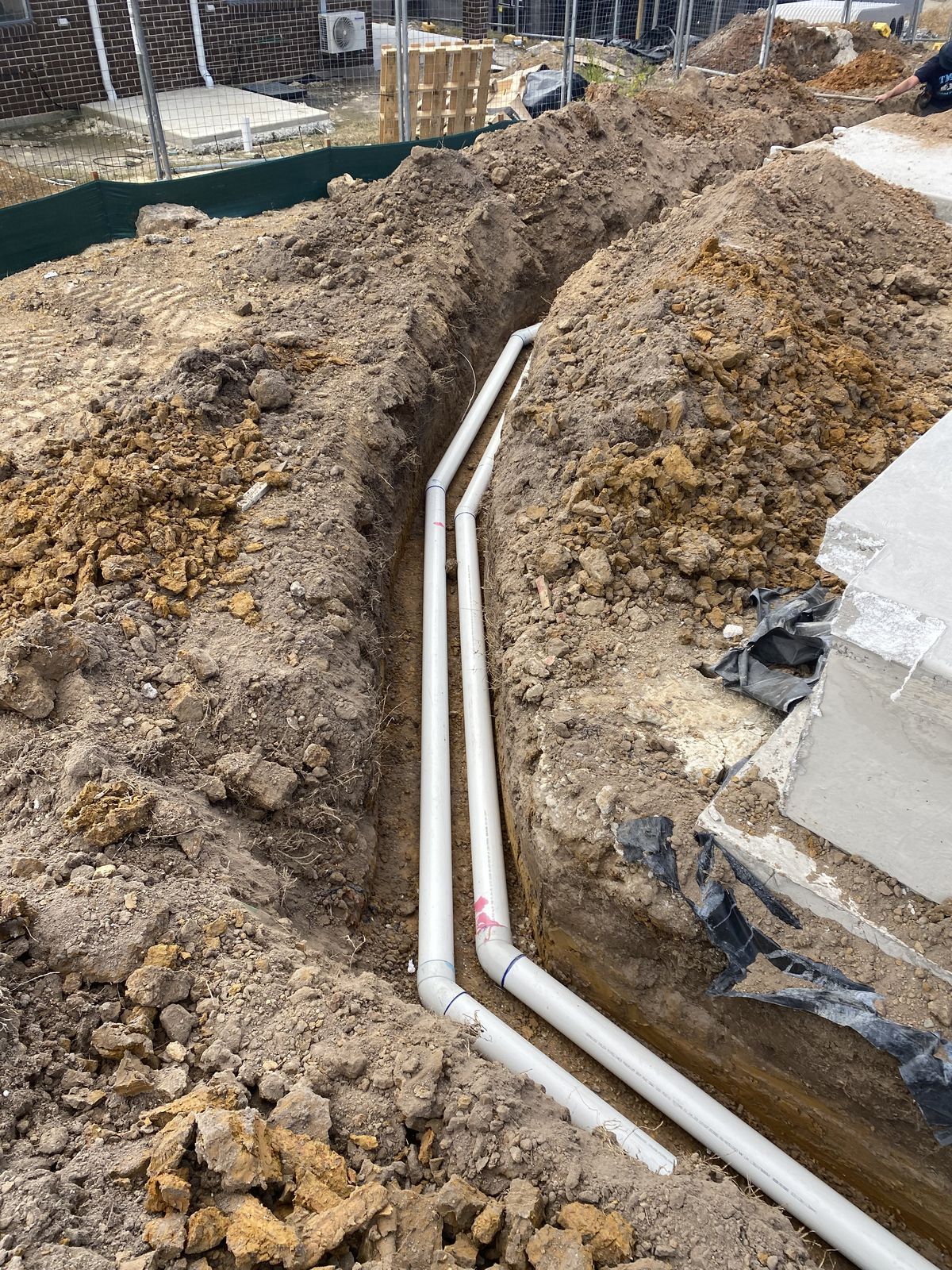 Two white PVC pipes running parallel along the bottom of an excavated dirt trench at a construction site.