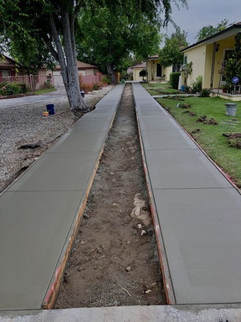 A concrete driveway ribbon installation under construction, featuring two parallel concrete strips with a dirt center.