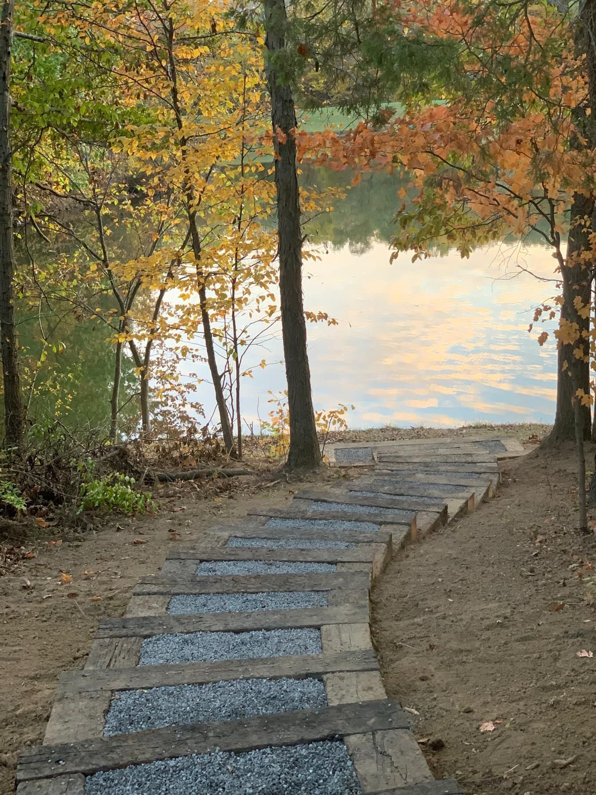 A wooden staircase leads down to a calm lake surrounded by trees with yellow and orange autumn foliage.