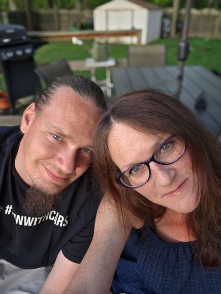 A man and a woman are posing for a picture together . the woman is wearing glasses.