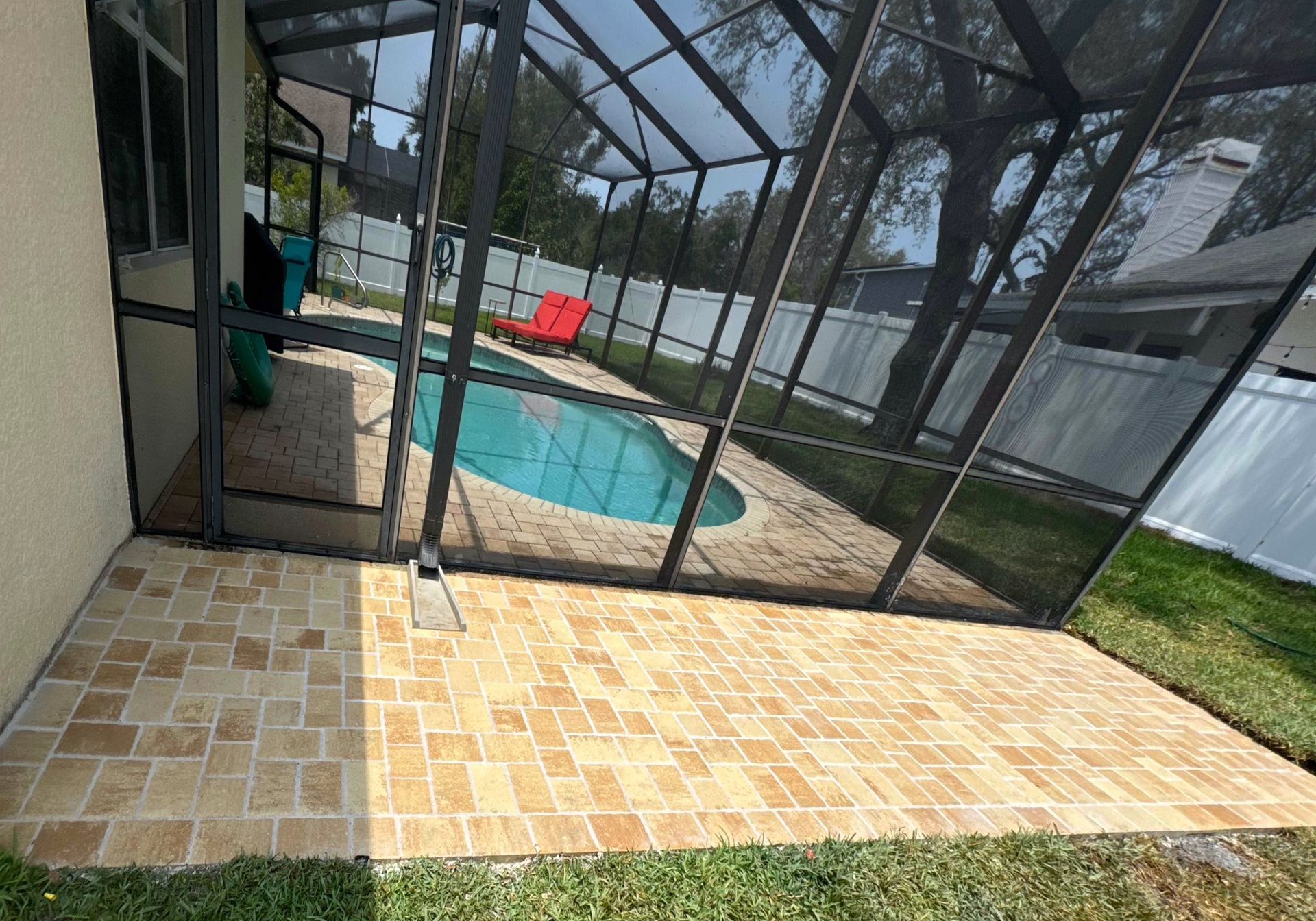 Pool enclosure attached to a house, with a pool visible inside. Green grass and trees are in the background.