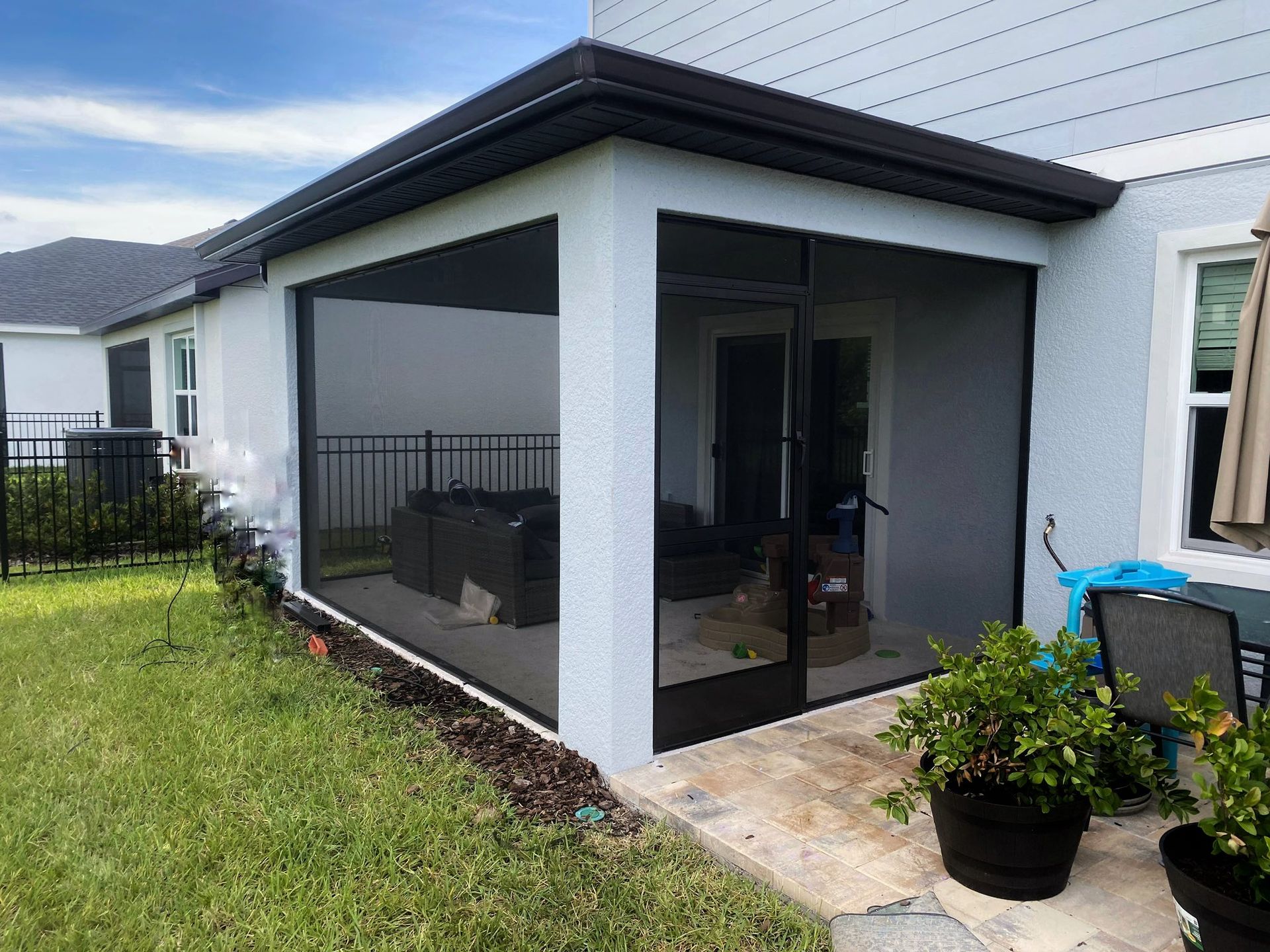 Sunroom with a glass roof and walls, furnished with a dining table, chairs, and a grill.