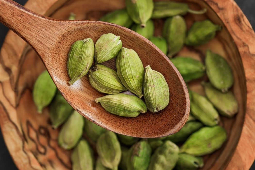 Wooden spoon holding green cardamom pods, bowl of cardamom.