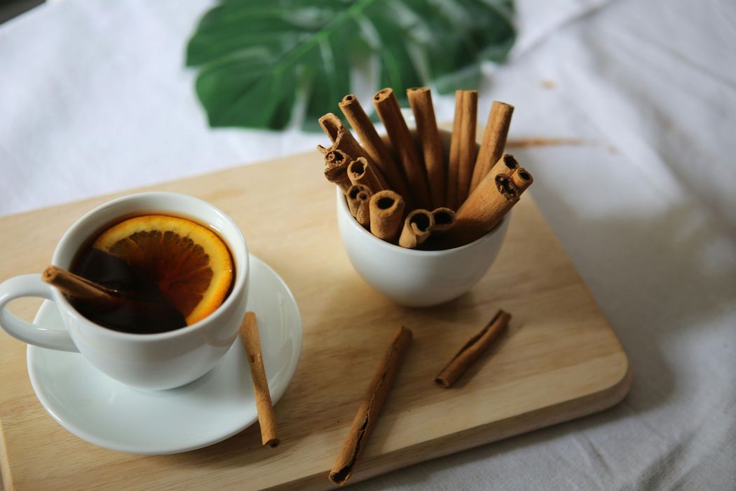 Cup of tea with orange slice and cinnamon sticks on wooden board.