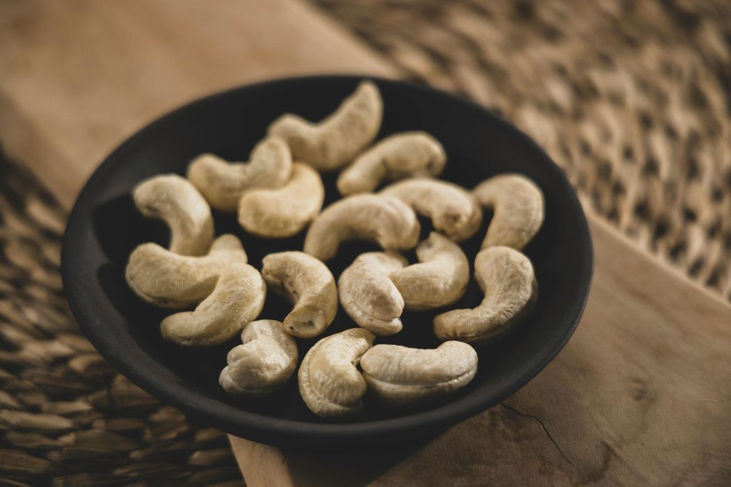 Cashew nuts in a black bowl on a wooden surface.