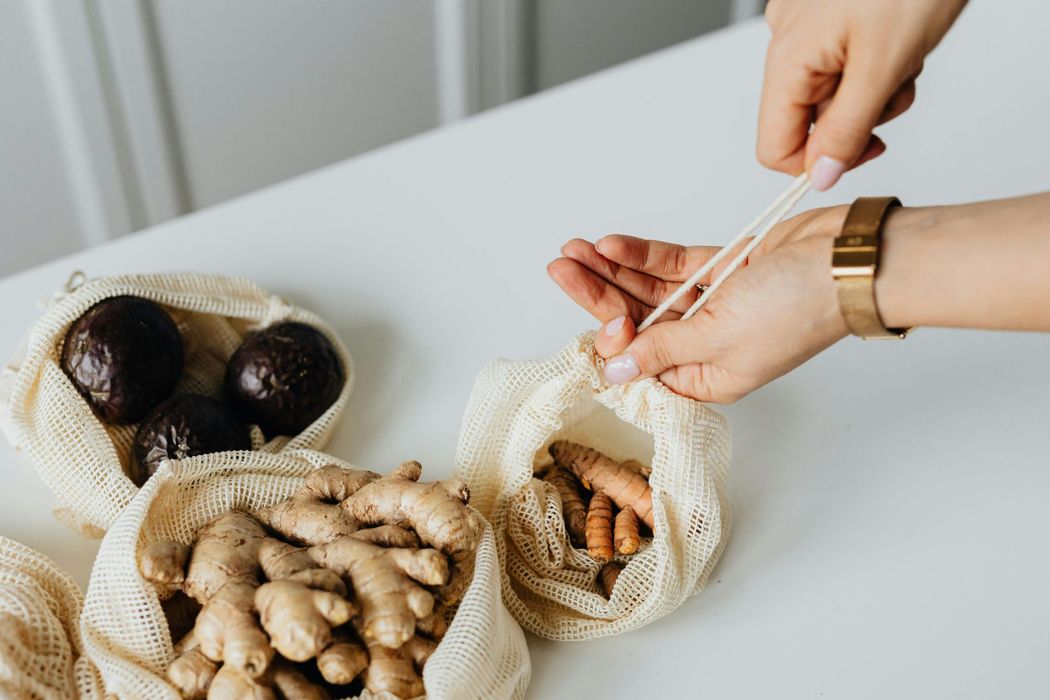 Person tying a drawstring bag filled with turmeric on a white table. Other produce bags are nearby.