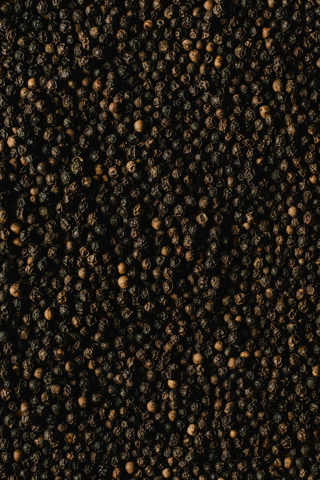 Black peppercorns, tightly packed, creating a textured, dark surface.