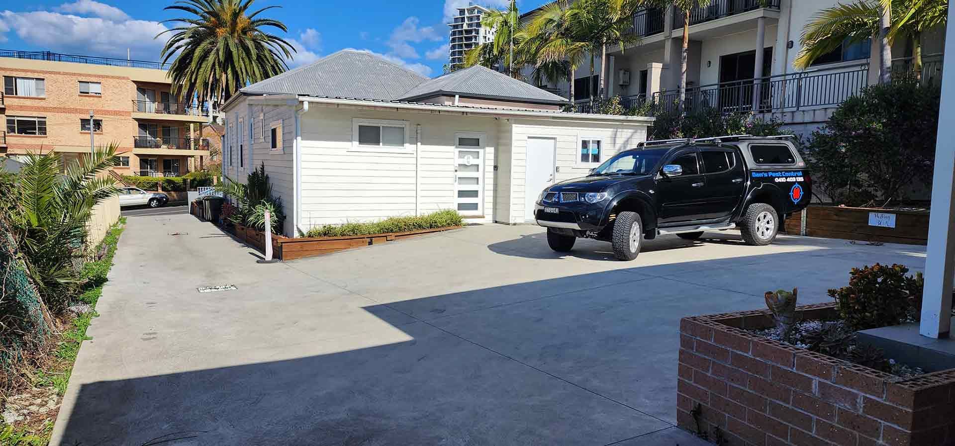 A Black Truck Is Parked In Front Of A White House — Dans Pest Control in Woonona, NSW
