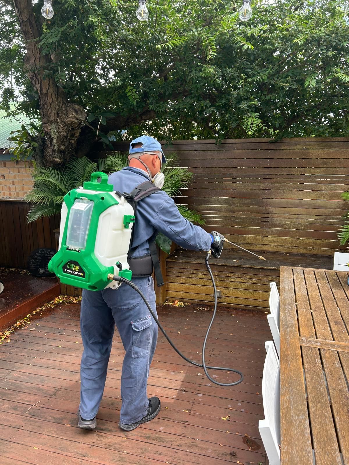 A Man is Spraying a Wooden Fence with a Sprayer — Dan’s Pest Control  in Woonona, NSW