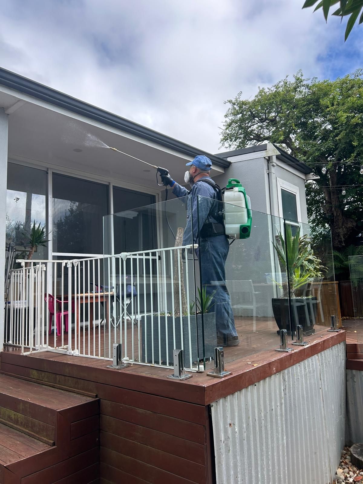 A Man is Spraying a House with a Sprayer — Dan’s Pest Control in Woonona, NSW