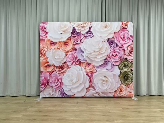 A wall of flowers is sitting on a wooden floor in front of a white curtain.