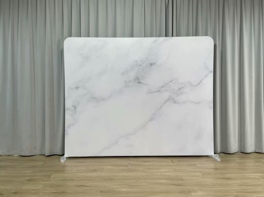 A white marble backdrop is sitting on a wooden floor in front of a white curtain.