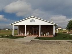 A one-story brick building with a porch, chairs, and a glass door under a cloudy sky.