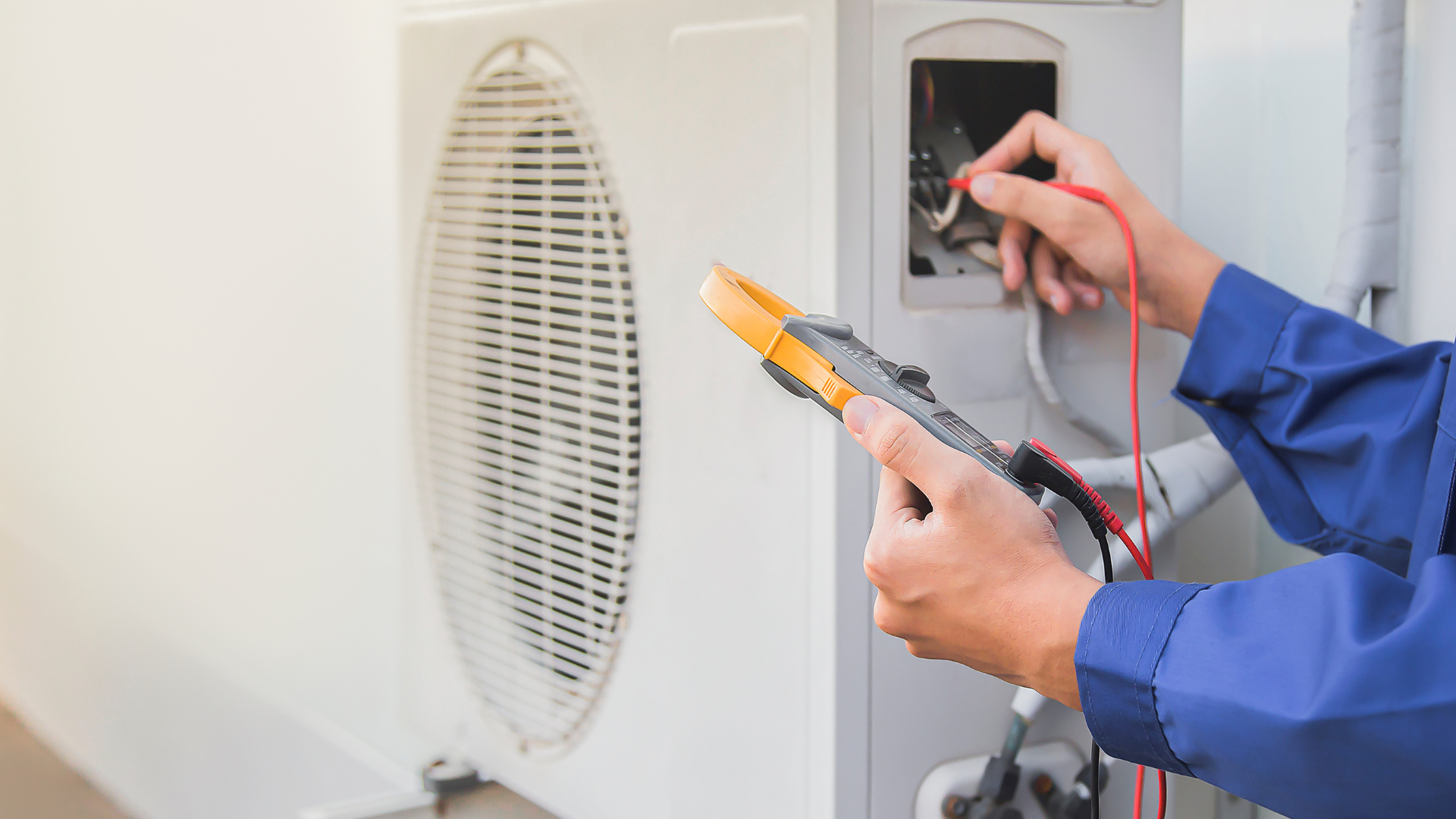 A man is using a multimeter to test an air conditioner.