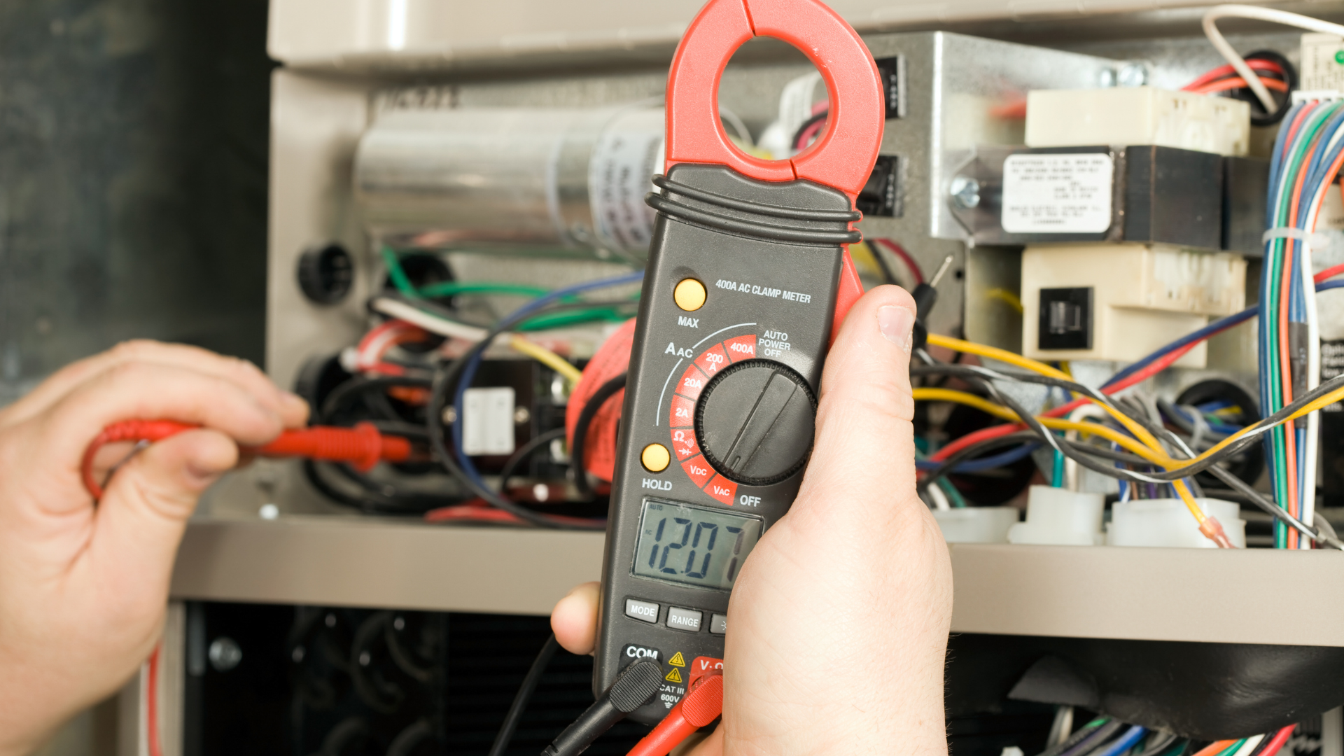 A person is holding a clamp meter in front of a machine.