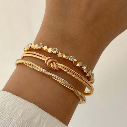Gold bracelets on a wrist, featuring gemstones, rope, and knot designs.
