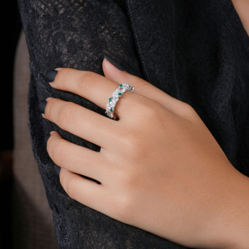 Close-up of a hand wearing a ring with white and green stones. The hand is in front of a dark garment.