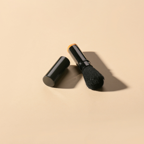 Black retractable makeup brush with cap on a beige surface.