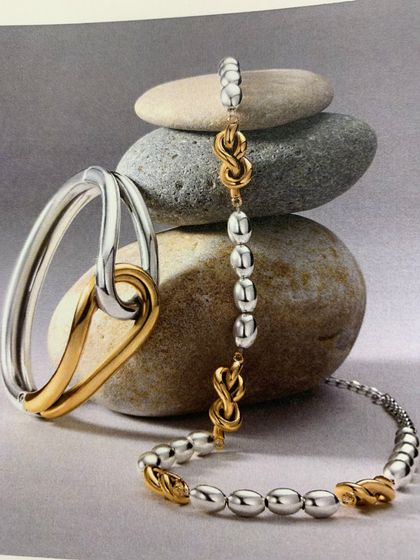 Woman's hand wearing a gold ring with a large oval, dark gemstone; hand near neck.
