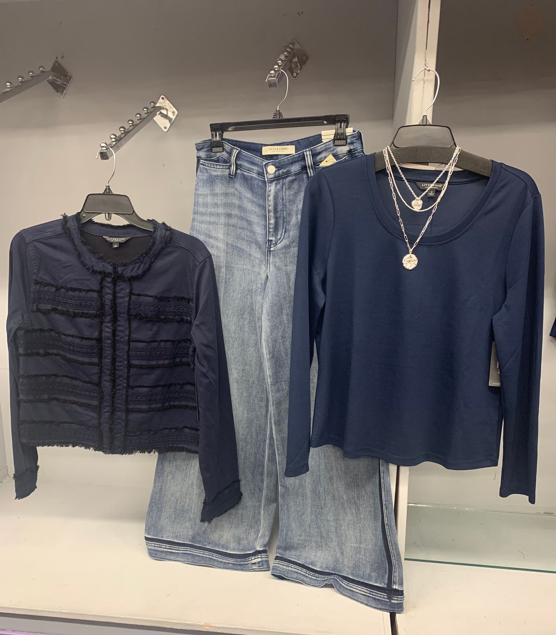 Clothes rack with pastel-colored apparel beneath a shelf with a plant and boot.