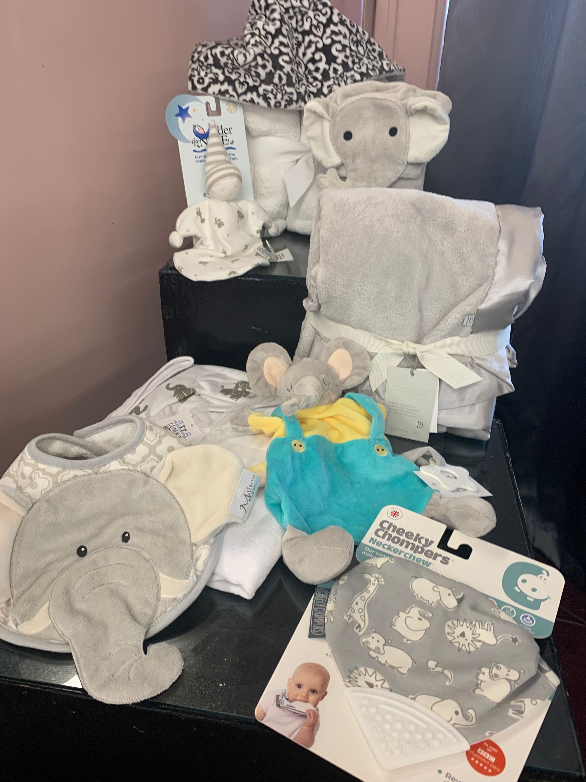Stacks of folded baby clothes on a sofa, including pink and blue items, next to a moon-shaped pillow.