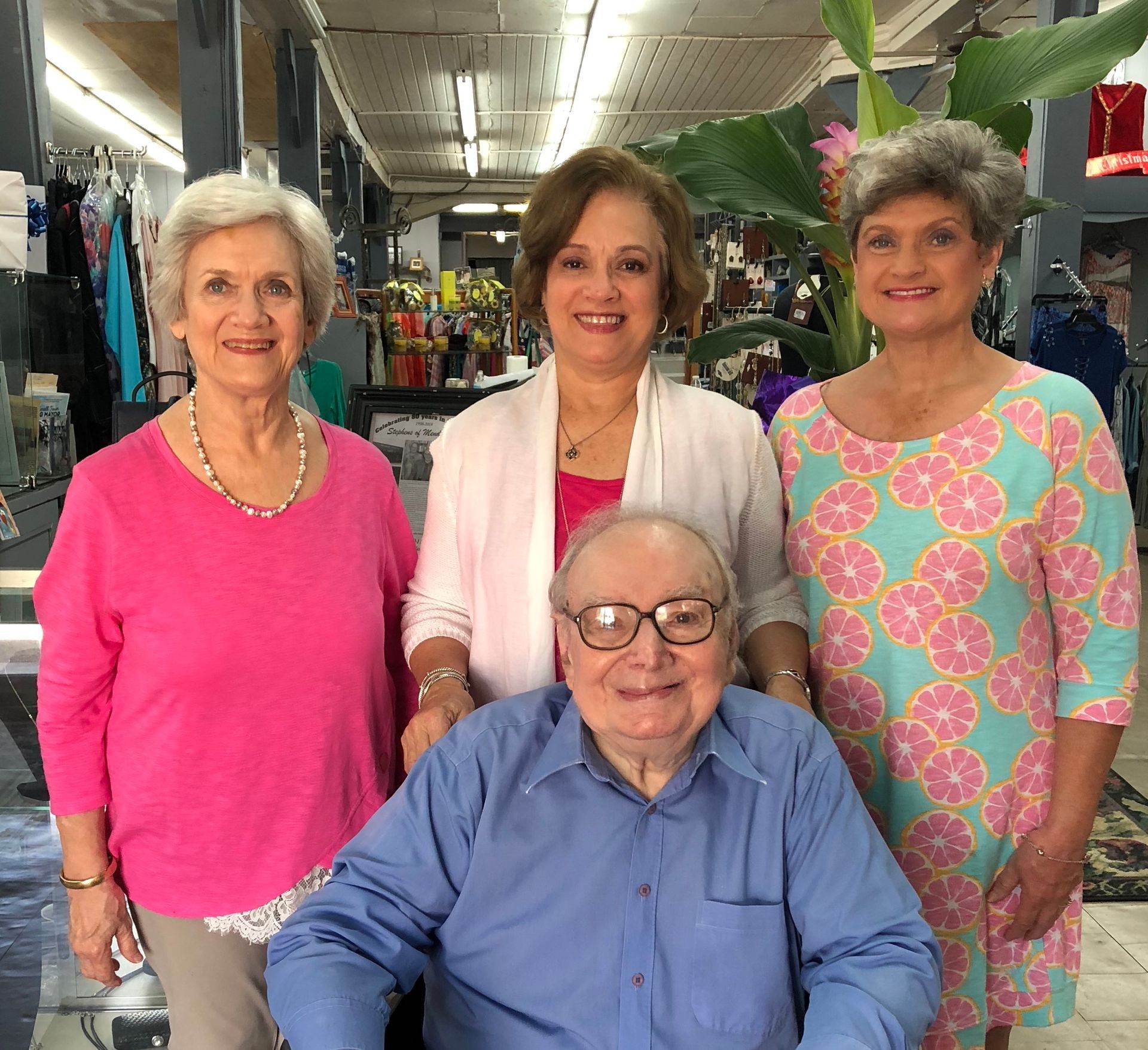 Group of four people posing indoors: three women standing, one man seated in wheelchair.