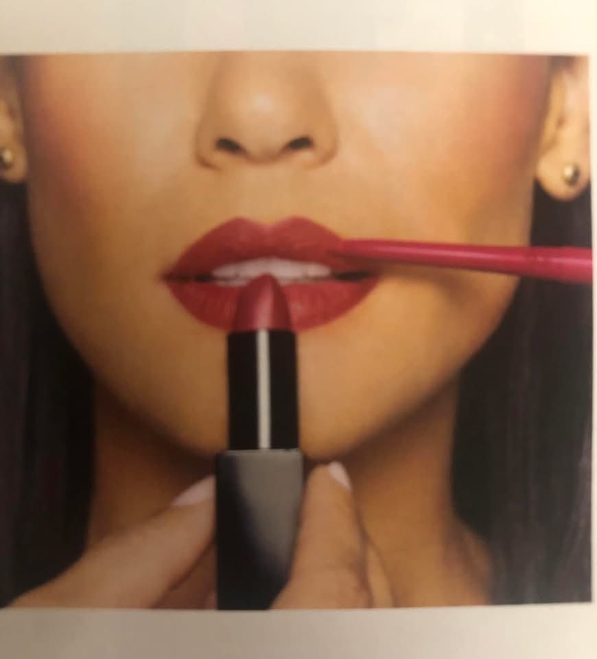 Person in a white robe applying pink cream from a small jar to their hand.