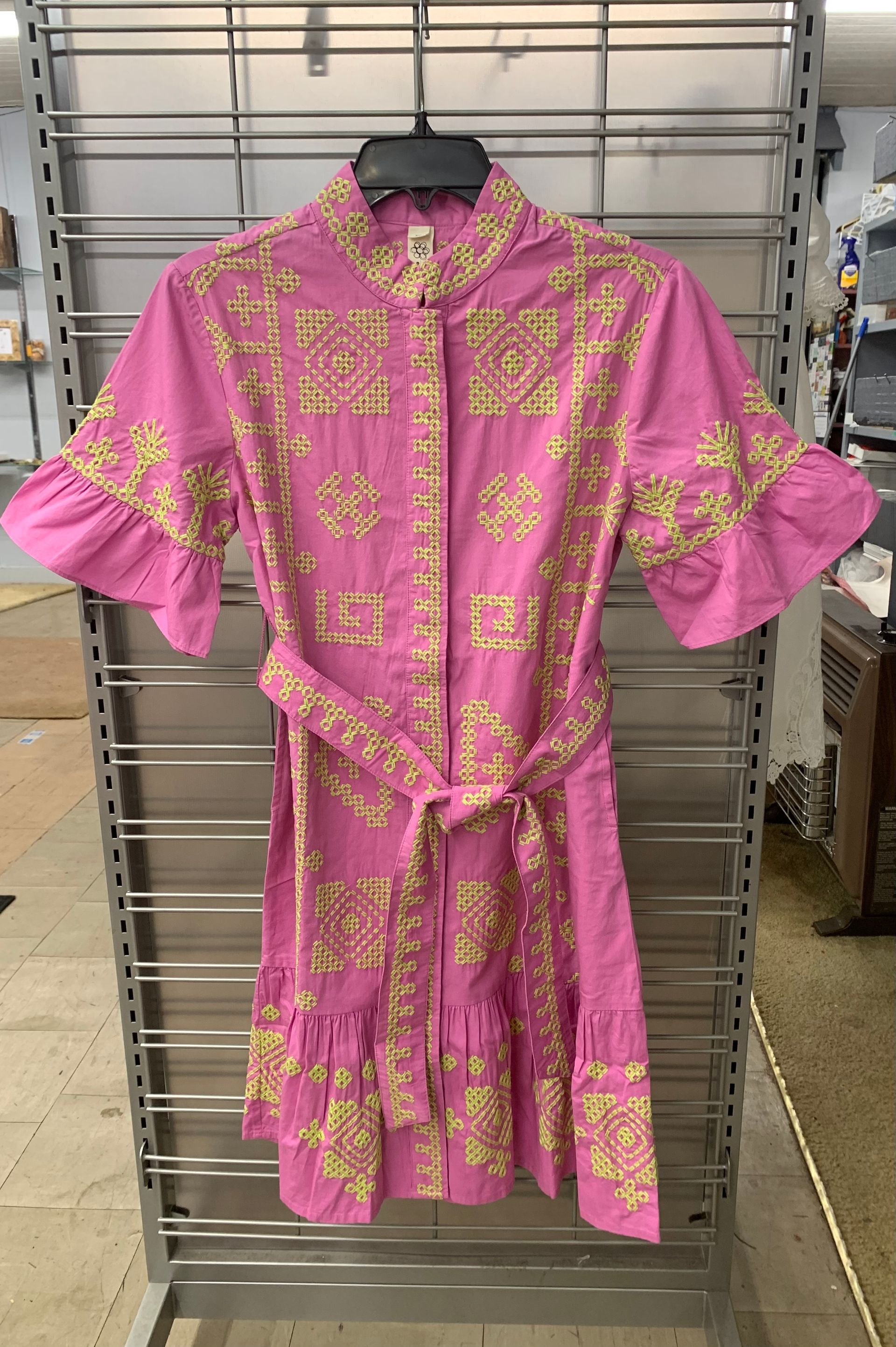 A pink, button-down short-sleeved dress with a yellow geometric pattern, a matching tie-belt, and a ruffled hem.