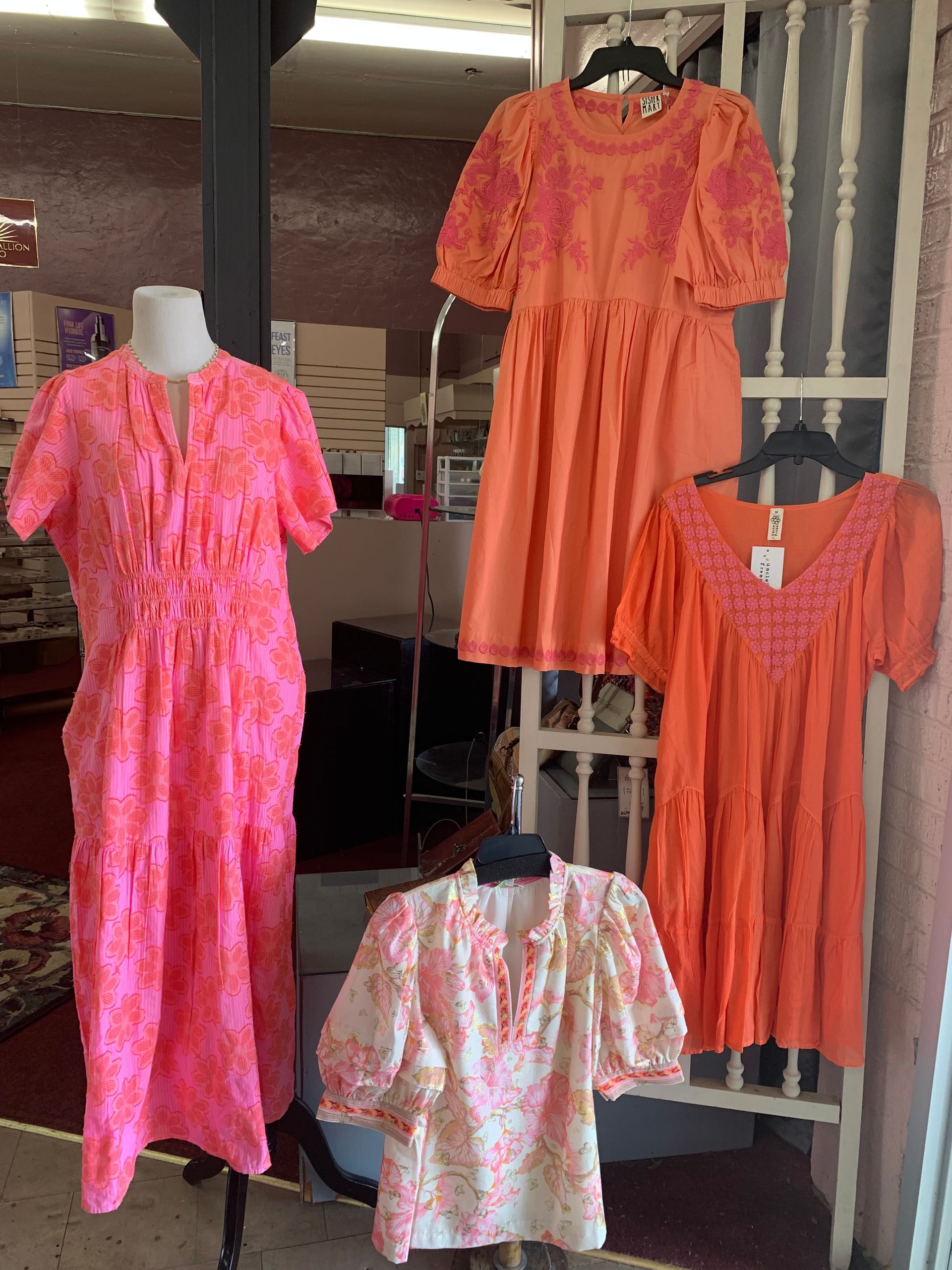 Four orange and pink dresses on mannequins displayed in front of a shop window