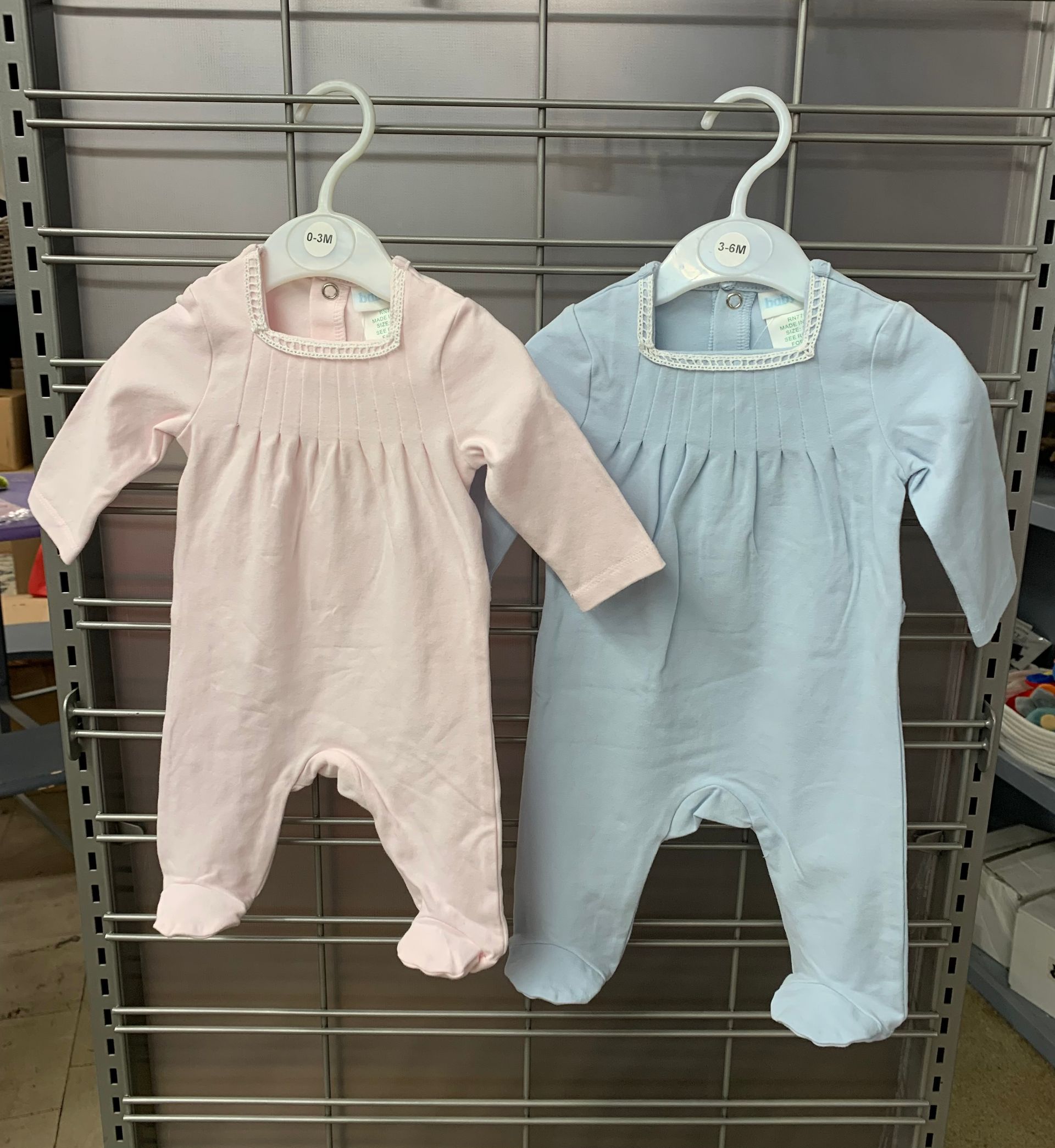 Three pink and white baby onesies layered on a cream-colored textured surface.