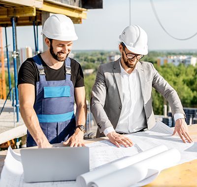 Two construction workers are looking at a laptop on a construction site.