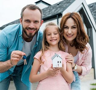 A smiling couple sits on the floor among moving boxes, with one person holding up keys to their new home.