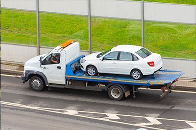 A white car is being towed by a tow truck.