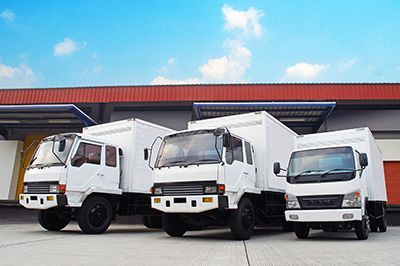 Three white trucks are parked in front of a warehouse.
